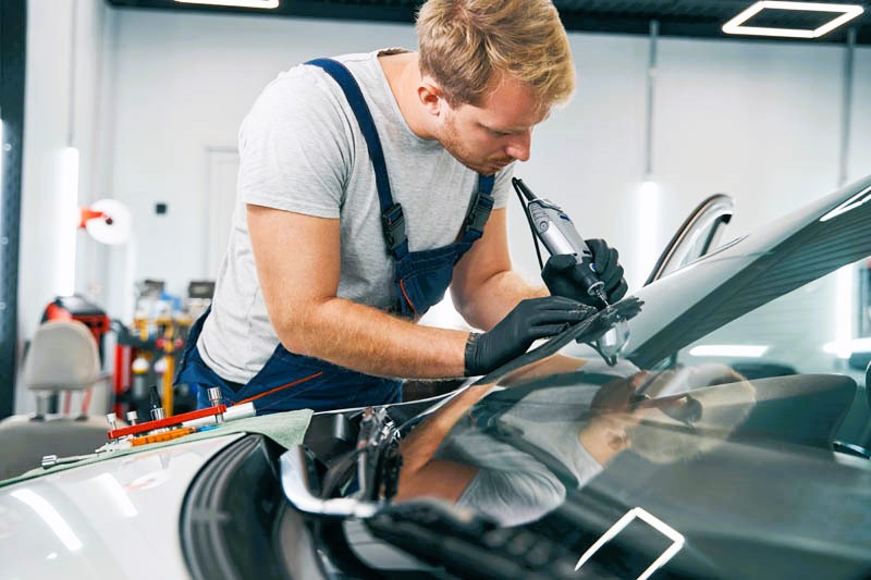 Car service technician checks crack on car windshield closeup