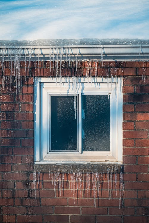 A Brown Brick House with Frozen Water During Winter