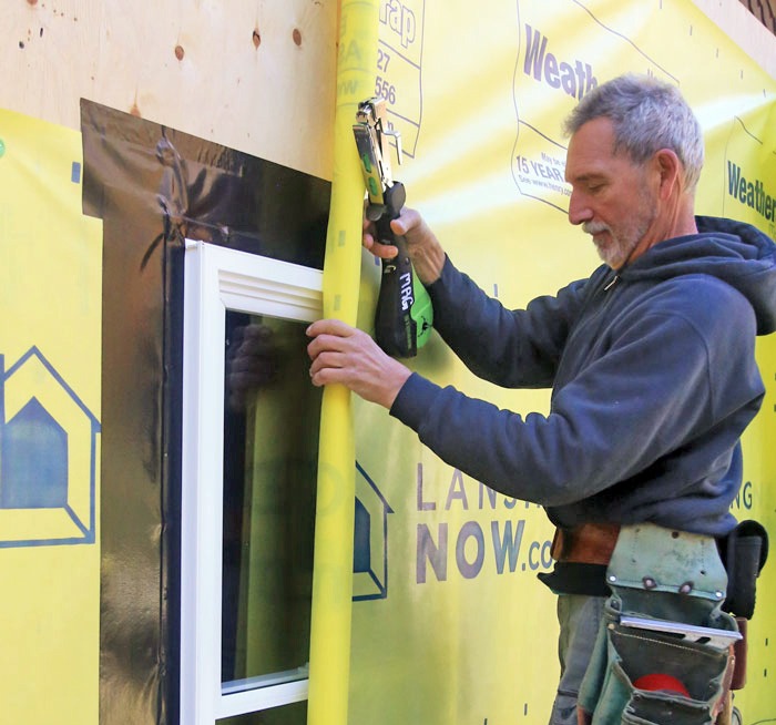 Contractor installing window with yellow weather barrier house wrap